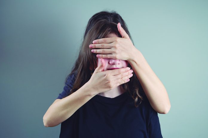 Close up portrait of teenage girl with covering eyes and mouth from mothers hands on gray background. Domestic violence