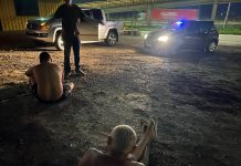 jovens sem camisa sentados no chão, algemado, de frente para um policial