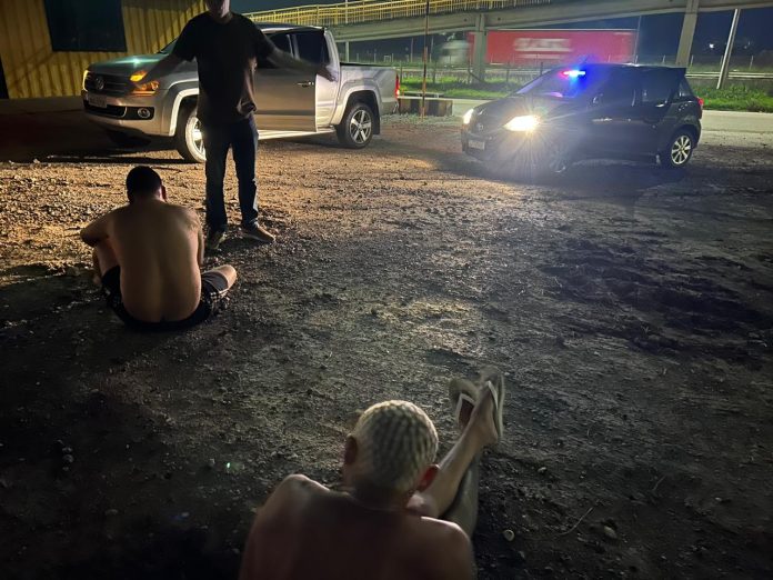 jovens sem camisa sentados no chão, algemado, de frente para um policial
